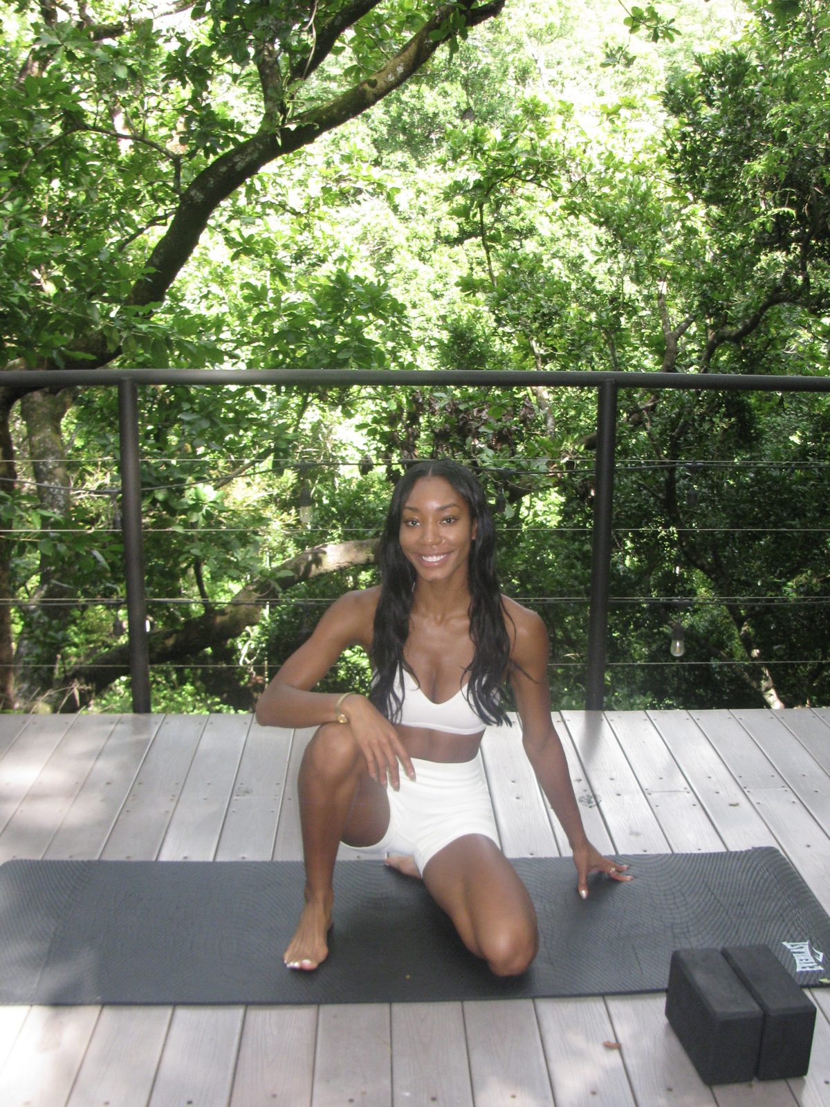 Maya in a yoga pose on a wooden deck surrounded by jungle